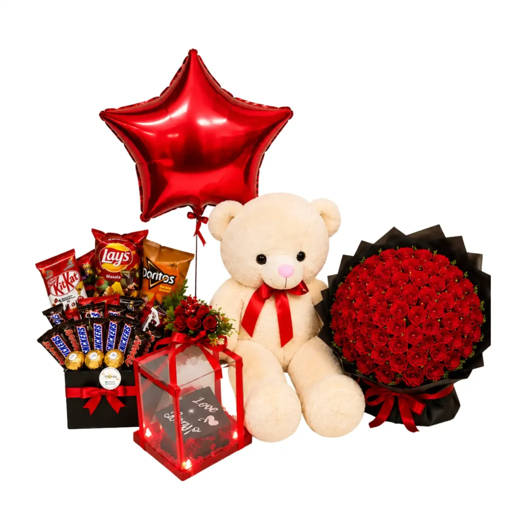 A teddy bear surrounded by red roses, a box of chocolates, and a star-shaped balloon, creating a romantic gift arrangement.