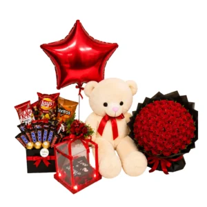 A teddy bear surrounded by red roses, a box of chocolates, and a star-shaped balloon, creating a romantic gift arrangement.