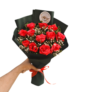 A hand holds a vibrant bouquet of red roses, showcasing their lush petals and green leaves.
